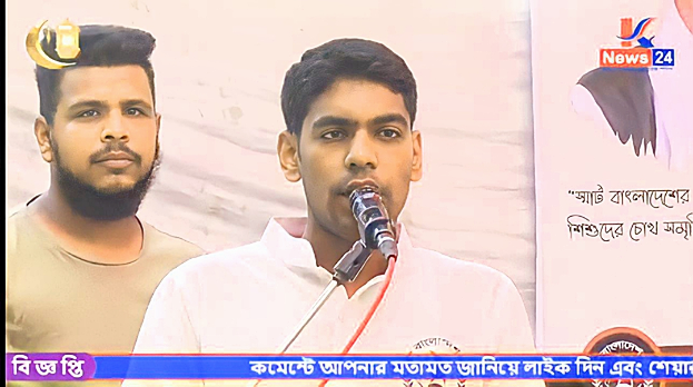 Zwei Männer stehen nebeneinander vor einem Fernseher, einer spricht in ein Mikrofon in einem weißen Hemd, der andere in einem hellgrauen T-Shirt, mit einem Banner und Logo dahinter und einem Watermark unten.