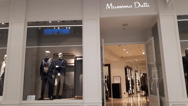 Innenansicht eines Massimo Dutti-Geschäfts in Mailand, Italien, mit Schaufensterpuppen in zeitgenössischer Kleidung, beleuchteter Decke, Informationsschildern und sichtbarem Boden.