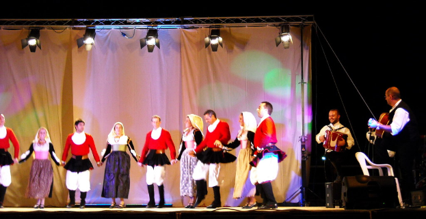 Eine Theateraufführung mit Darstellern, Musikern auf der rechten Seite, einem Vorhang im Hintergrund, Scheinwerfern oben und einem weißen Stuhl in der unteren rechten Ecke.