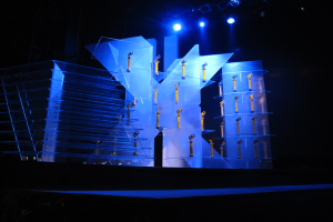 Bühne für eine Preisverleihung mit dunklem Hintergrund, beleuchtet von ein paar Lichtern, mit Gegenständen, die wahrscheinlich mit dem Ereignis in Verbindung stehen.