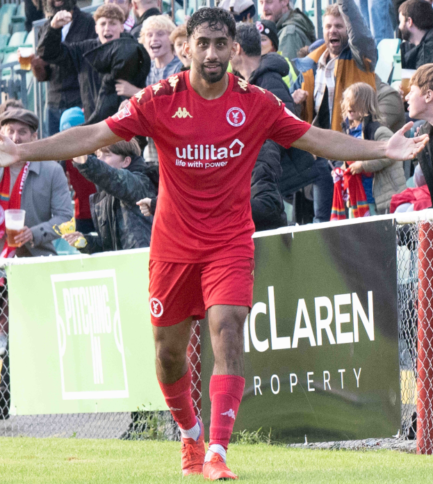 Ein Fussballspieler in roter Uniform rennt mit ausgebreiteten Armen auf einem Feld, mit einer Menge im Hintergrund und einem Banner mit der Aufschrift "Middlesbrough FC v Swansea City - Sky Bet Championship" im Vordergrund.