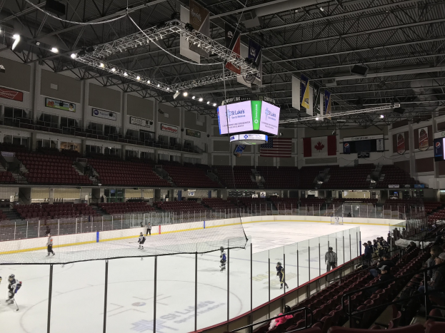 Eishockeyspiel in einer großen Arena mit einem zentralen Netz, Zuschauern auf Stühlen, Deckenbeleuchtung und Trägern sowie Bannern an den Wänden, die 'St. Louis Blues Arena' beschriften.