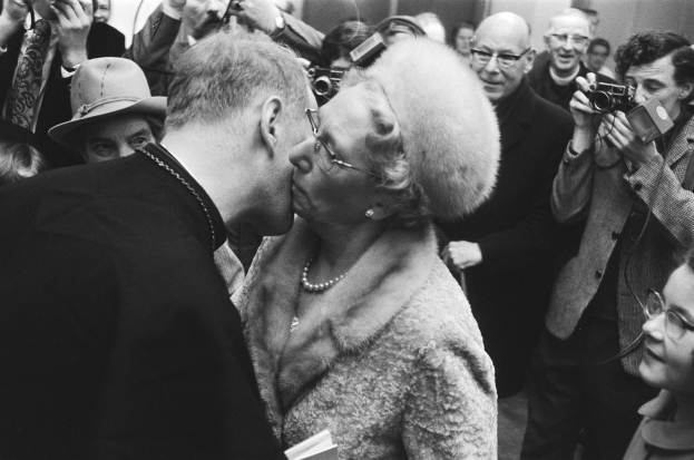 Schwarzes und weißes Foto eines Mannes und einer Frau, die sich küssend umarmen, umgeben von einer Menge mit Kameras.