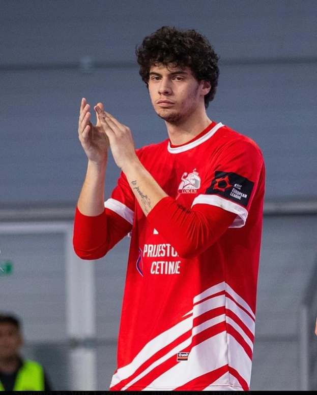 Ein Mann in rot-weißem T-Shirt klatscht in den Händen im Vordergrund, mit einer anderen Person und einer Wand im Hintergrund, und Text unten lesend "Copenhagen Futsal Club - Foto 1".