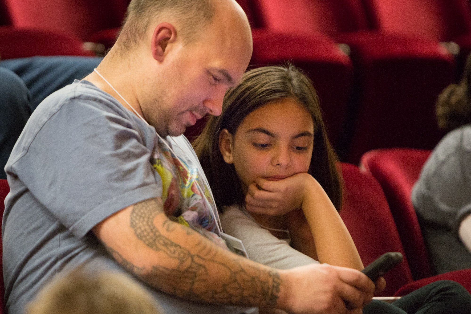 Zwei Menschen in einem Kino, ein Mann und ein junges Mädchen, das auf ein Handy schaut, das der Mann hält.