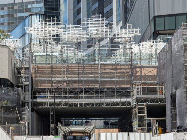 Großes Gebäude mit Gerüst, das renoviert wird, umgeben von Bäumen auf der linken Seite und einer Straße unten in einer städtischen Umgebung.