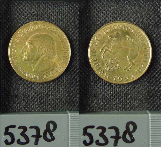 Zwei Goldmünzen aus Deutschland im Jahr 1922, jeweils mit einem Nennwert von 100 Mark, werden auf einer schwarzen Oberfläche mit Zahlen unten plaziert.