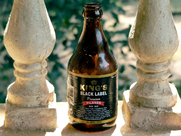 Eine schwarze Flasche der King's Marke ist zwischen zwei unbestimmten Gegenständen platziert.