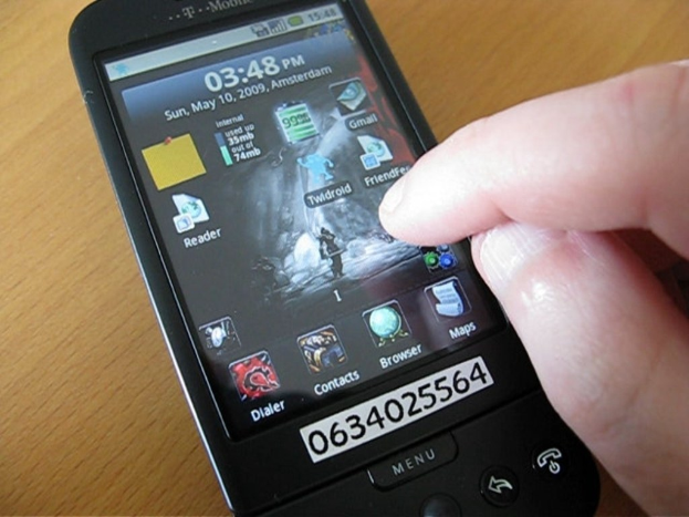 Mobiltelefon mit Apps auf dem Display, eine Telefonnummer auf einem Zettel, der am Telefon befestigt ist, und das Telefon auf einem Tisch.