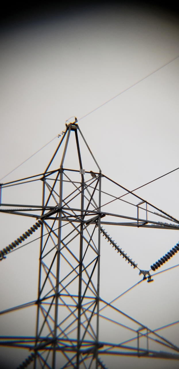 Ein hoher Strommast mit mehreren Drähten vor einem klaren, tiefblauen Himmel.