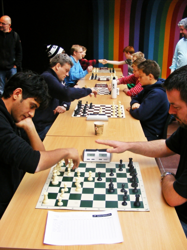 Zwei Personen sitzen sich an einem Tisch gegenüber und spielen Schach mit einem Sichtbaren Timer.