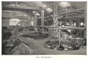 Schwarzes und weißes Foto einer historischen deutschen Fabrik mit Arbeitern, die an Maschinen arbeiten, umgeben von Metallstangen und Polen, beschriftet mit "Neue Eisengießerei, die erste Fabrik in Deutschland" unten.