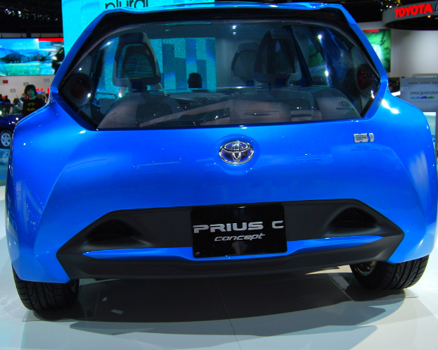 Ein blaues Auto im Vordergrund mit einer Gruppe von Menschen, Schildern und einem weiteren Auto im Hintergrund.