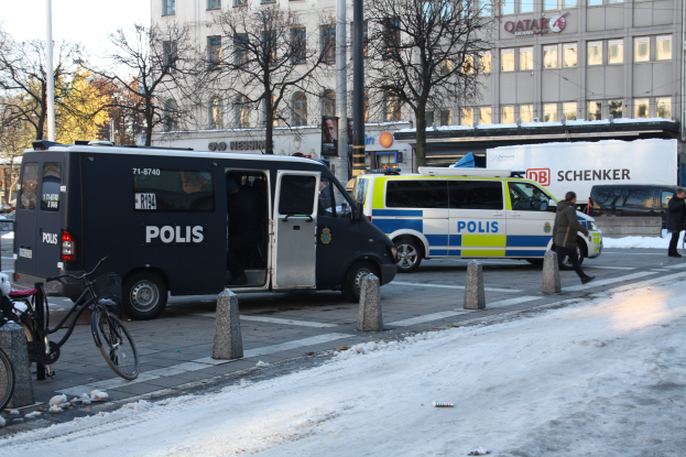 Ein Polizeiwagen steht an der Seite einer verschneiten Straße mit Fahrzeugen auf der Straße, Fußgängern auf dem Gehweg und Fahrrädern in der Nähe, mit Bäumen, Polen, Gebäuden und einem klaren Himmel im Hintergrund.