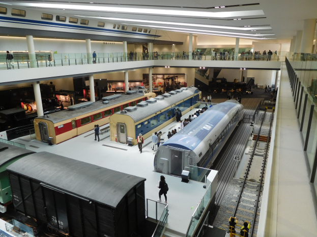 Ein großer Museumsraum mit verschiedenen Bahnen in unterschiedlichen Größen und Farben, die von Menschen auf verschiedenen Ebenen betrachtet werden.