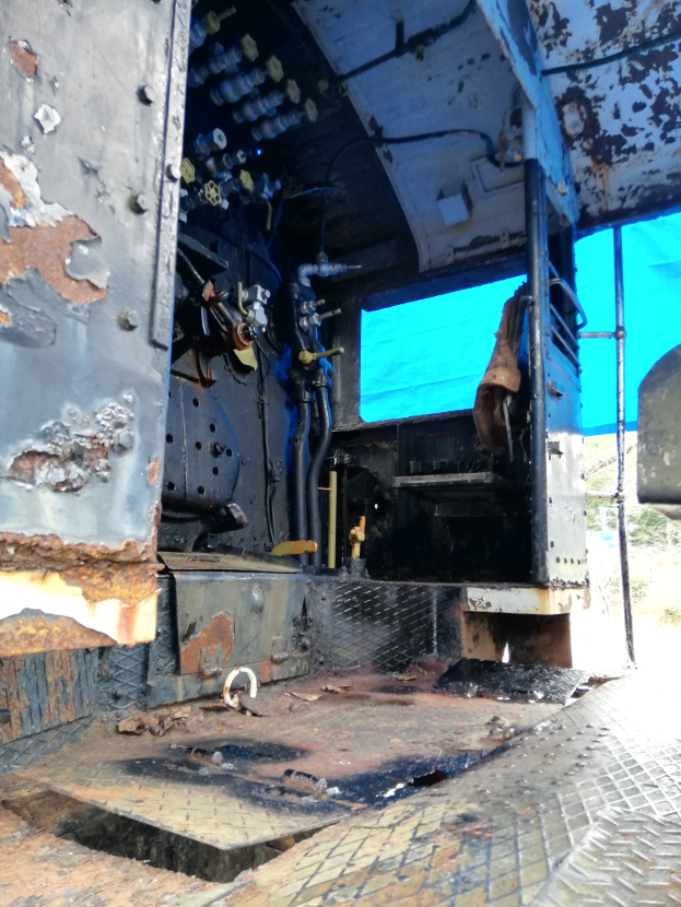 Das Innere eines verrosteten, baufälligen Lastwagens mit Bäumen und einem klaren blauen Himmel im Hintergrund.