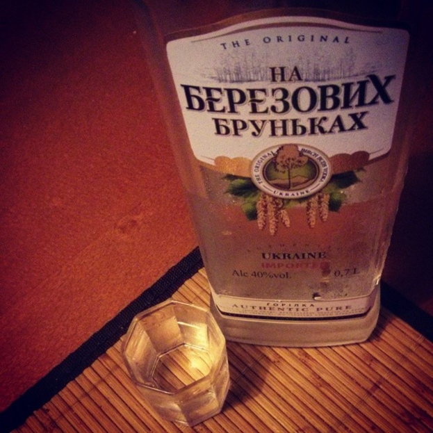 Ein klares Glas mit einer goldenen Flüssigkeit, wahrscheinlich Alkohol, das auf einer beigen Matte steht.