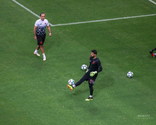 Mann in Sportuniform kickt Fußball auf grünem Rasen.