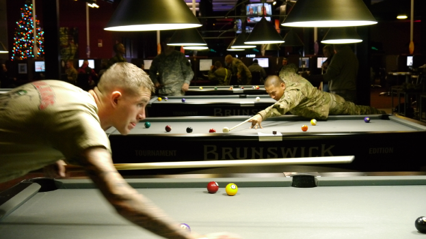 Ein Raum mit Snookertischen, Spielern auf beiden Seiten, hängenden Lampen, einem Weihnachtsbaum in der Ecke und Bildschirmen mit Ergebnissen.
