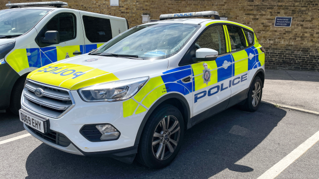 Zwei Polizeiwagen nebeneinander auf einem Parkplatz geparkt, mit einer Wand und einer Texttafel im Hintergrund.