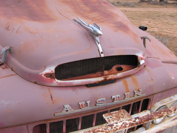 Alter rostiger Lkw auf einem Feld mit Bäumen und einem klaren blauen Himmel.