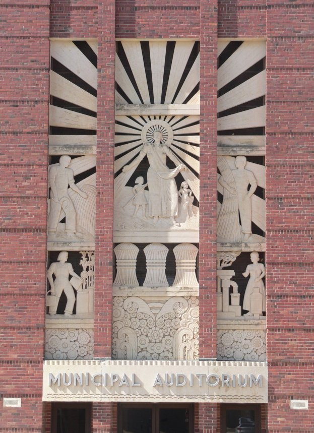 Außenansicht eines Backsteingebäudes mit der Aufschrift "Municipal Auditorium" und dekorativen Verzierungen, mit Türen an der Basis, die zum Eingang führen.