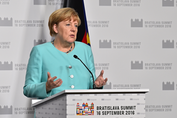 Bundeskanzlerin Angela Merkel hält eine Rede auf dem Bratislava-Gipfel, stehend an einem Pult mit zwei Mikrofonen, mit einem Banner und einer Flagge dahinter.