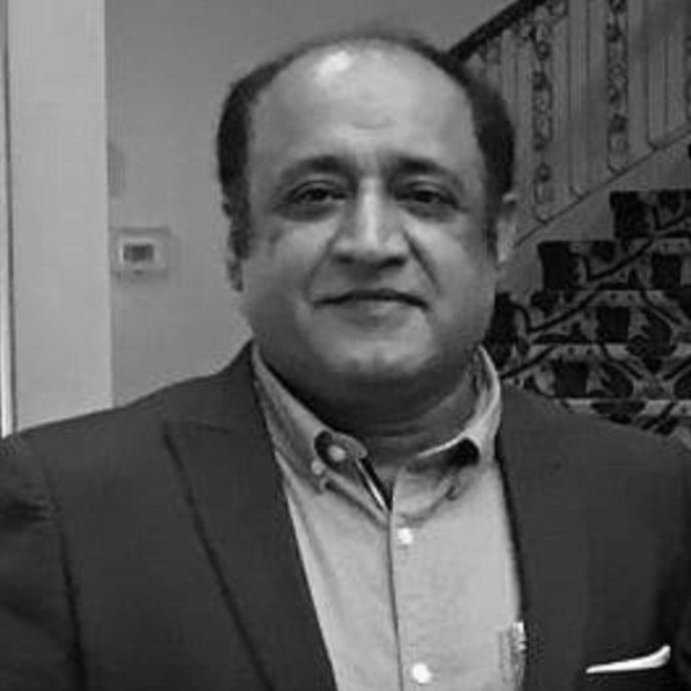 Ein Mann in einem Anzug steht vor einer Treppe und sieht besorgt aus, mit einer Wand im Hintergrund, auf einem Schwarz-Weiß-Bild.