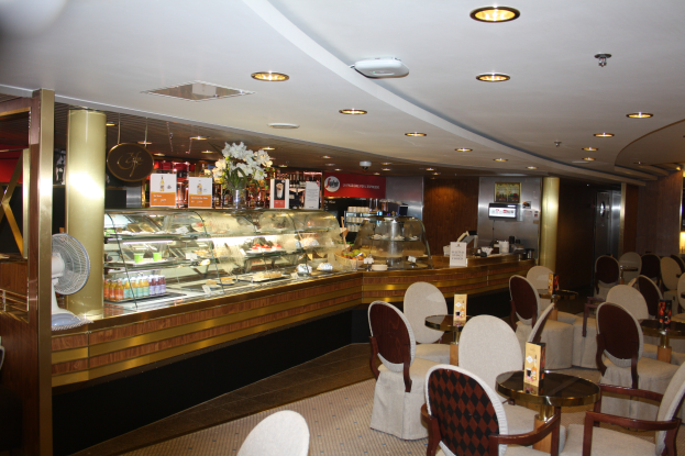 Ein Restaurant-Innenraum mit Tischen und Stühlen, einer Theke mit Blumenvasen, Schildern mit Text, einem Ventilator und anderen Gegenständen unter einer Decke, die mit warmen Lichtern beleuchtet ist.