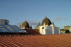 Stadtansicht mit mehreren Gebäuden im Vordergrund und einem klaren blauen Himmel im Hintergrund, mit Solarpanelen auf dem Dach eines Gebäudes.