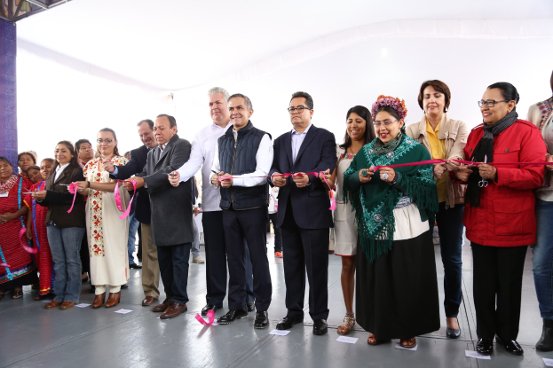 Gruppe von Menschen bei einer Scherenschnittzeremonie, die Schere haltend, vor einer Menge mit Papieren auf dem Boden und einem weißen Tuch im Hintergrund.